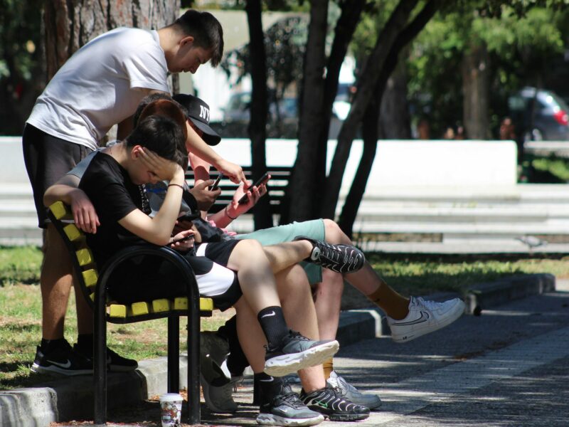 The youth spending time outside together, but focused on their digital screens.