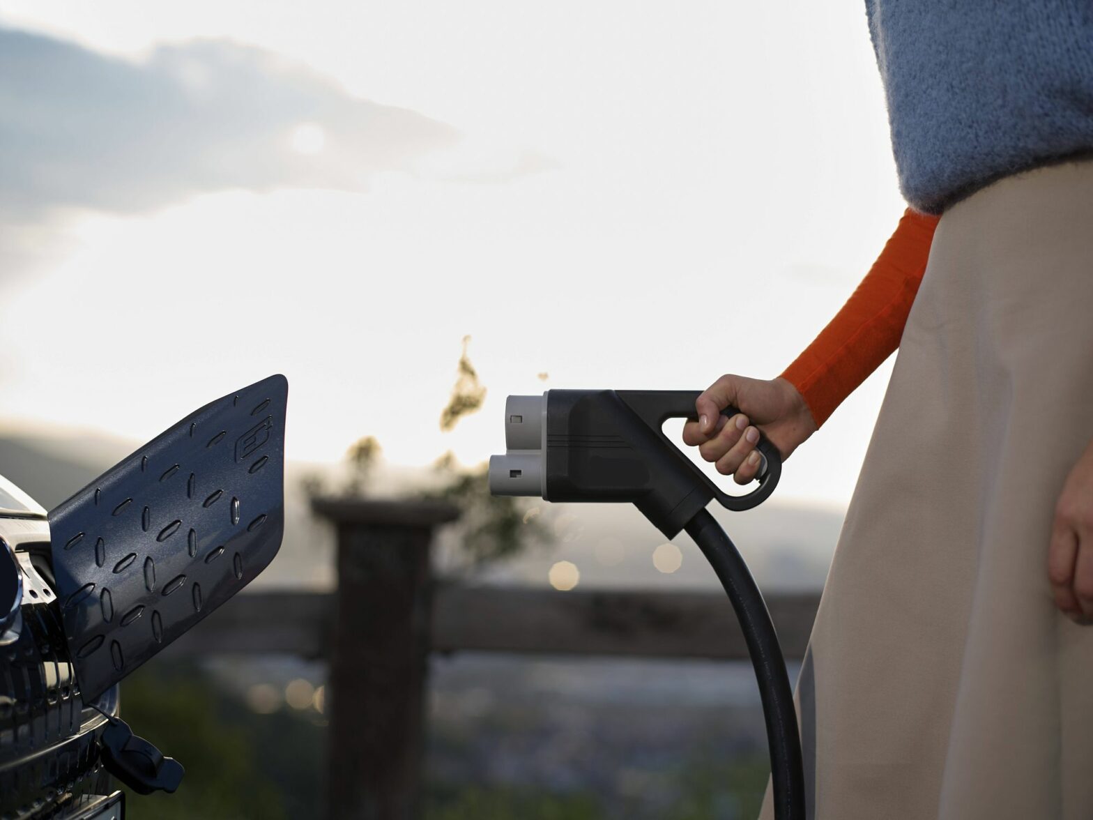 There's a pretty good chance the battery of the Electric Car you are charging was manufactured in China: their EV production industry accounts for around 58% of global production. Picture of a woman charging an EV.