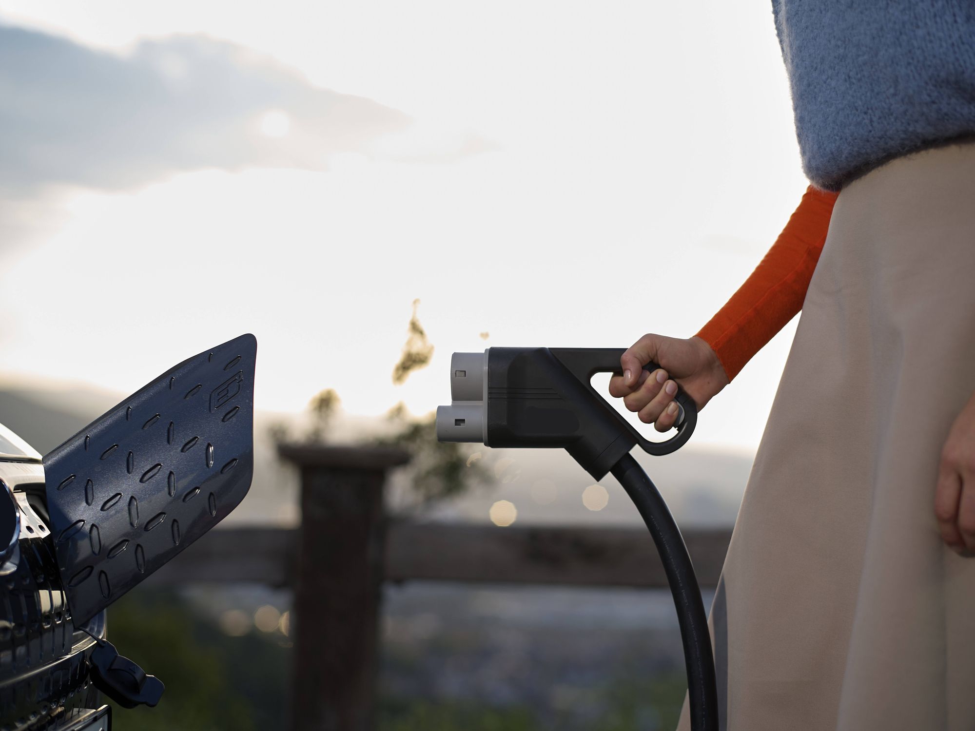 There's a pretty good chance the battery of the Electric Car you are charging was manufactured in China: their EV production industry accounts for around 58% of global production. Picture of a woman charging an EV.