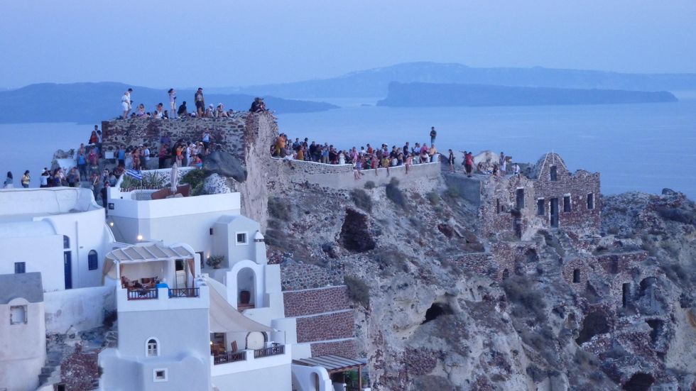 This is a photo of a Santorini cliff where tourists stand and watch the sunset.