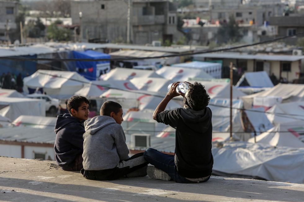 Three displaced Palestinian childrendrinking water take shelter in a makeshit tent camp near the Kerem Shalom crossing borde