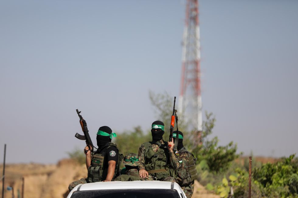 Three fighters from he Izz al-Din al-Qassam Brigades, the military wing of Hamas, sit on the roof of a car with rifles during a military parade.