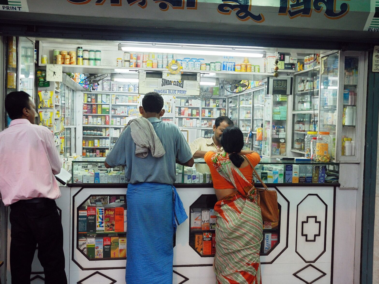 Three people stand in front of the counter of a pharma stand.