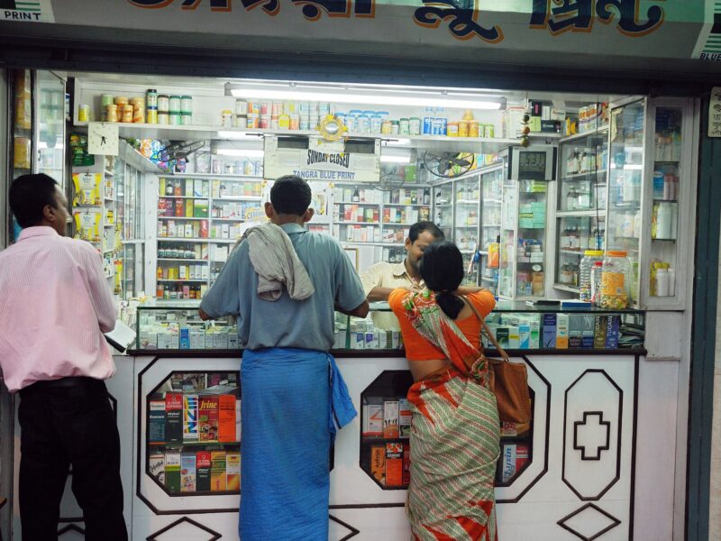 Three people stand in front of the counter of a pharma stand.
