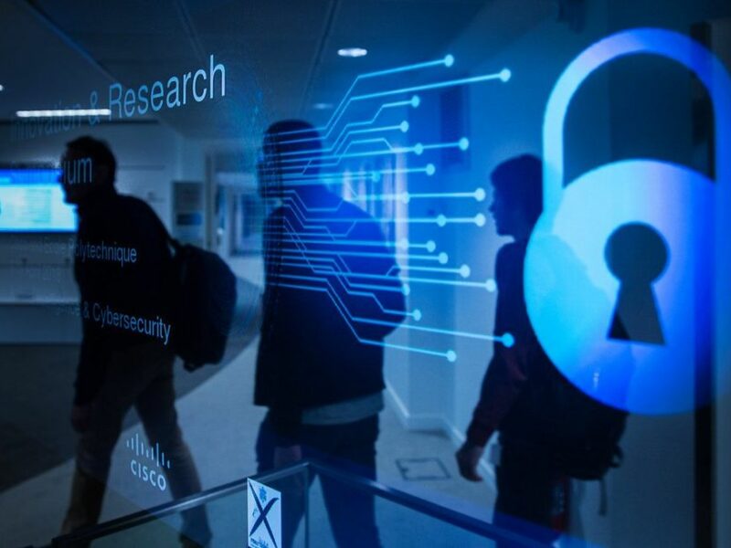 Three silhouettes with backpacks overlaid by a blue transparent cybersecurity screen.