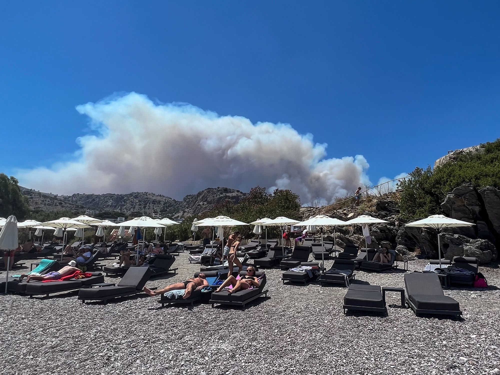 Tourist sunbathe as smoke from wildfire's looms behind them on the Greek island of Rhodes.