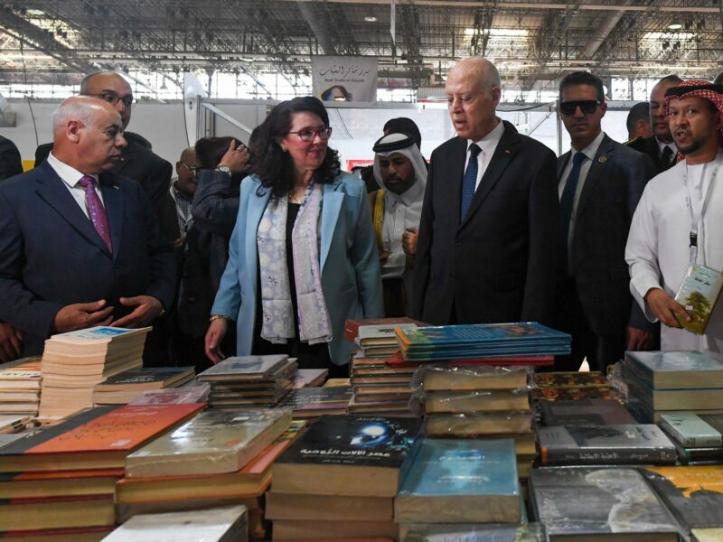 Tunisian President Kais Said and his entourage stand infront of a table piled with books