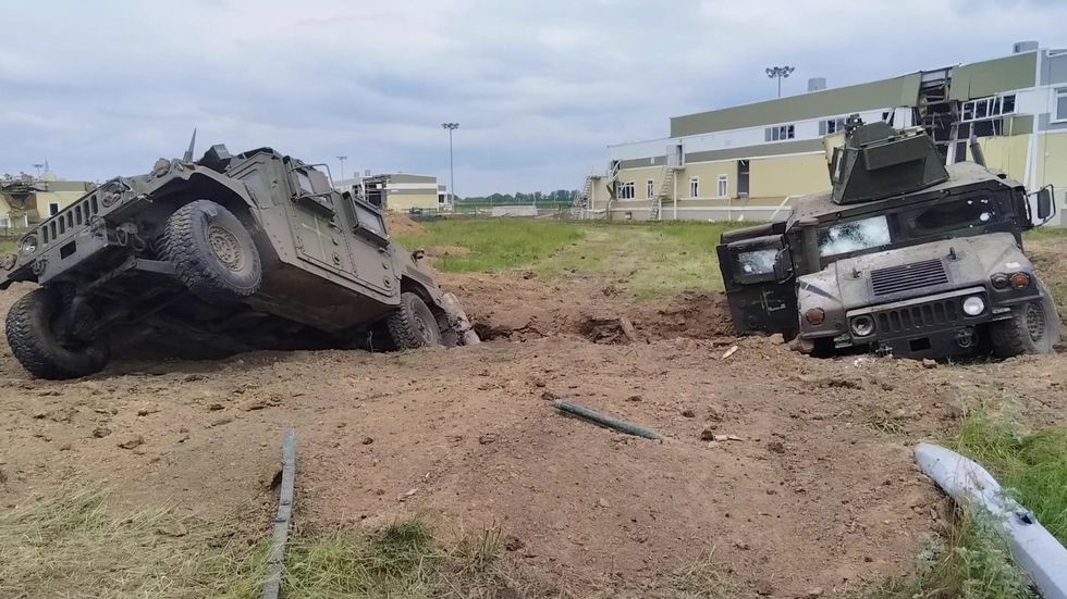 Two armoured vehicles with white graffiti abandoned in a muddy ditch infront of some buildings