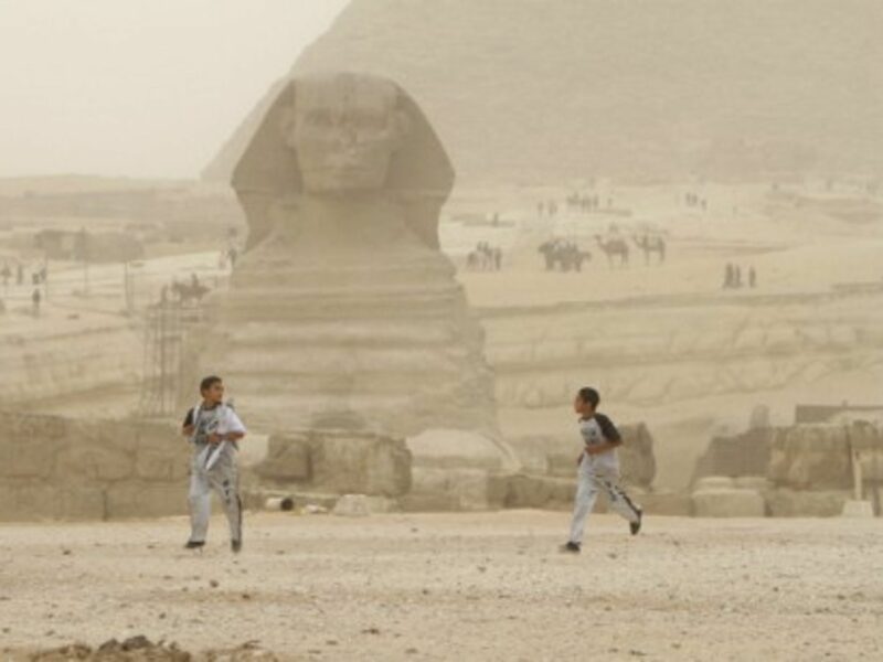 Two boys run in front of the great sphinx of Giza