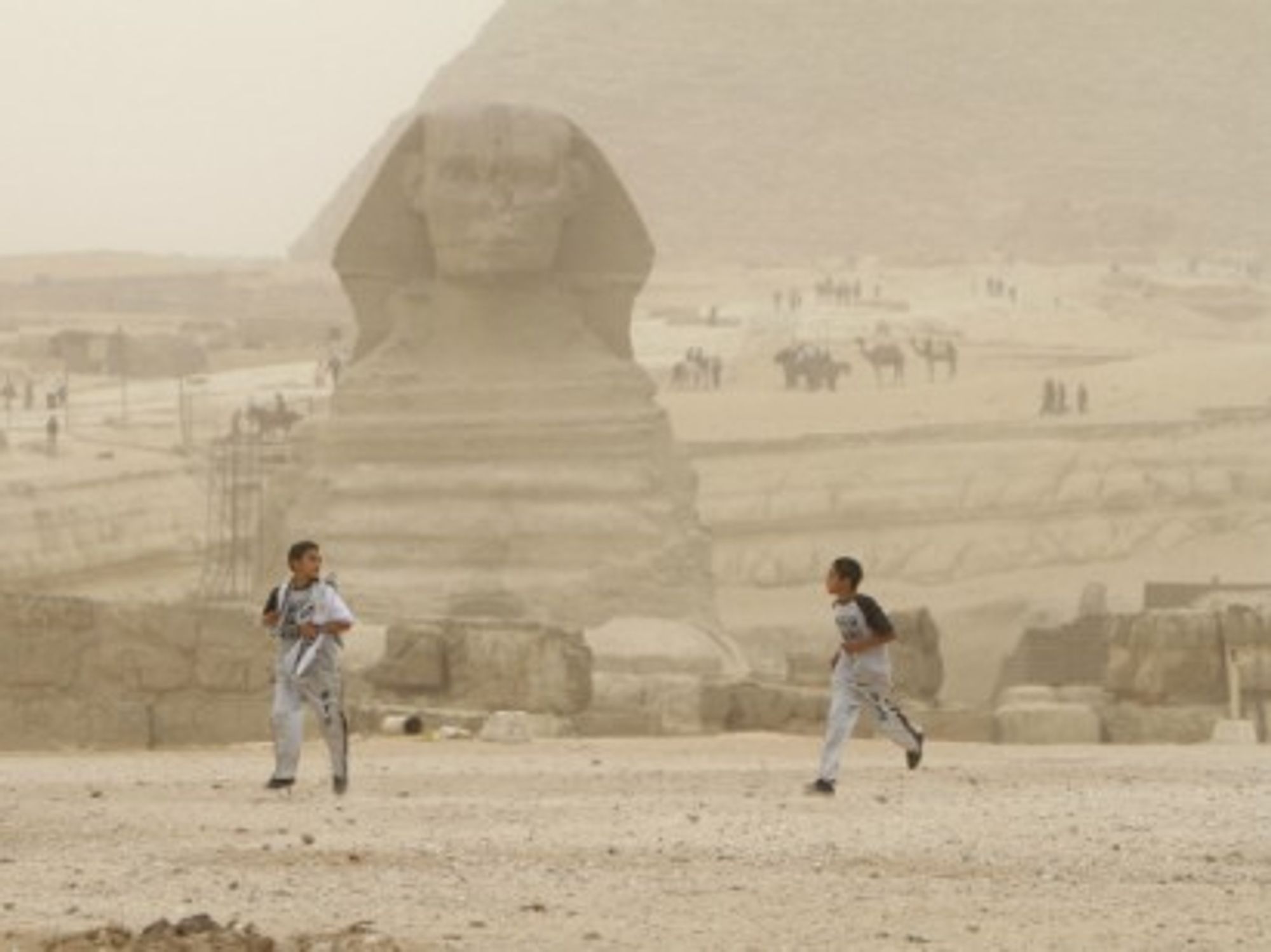Two boys run in front of the great sphinx of Giza