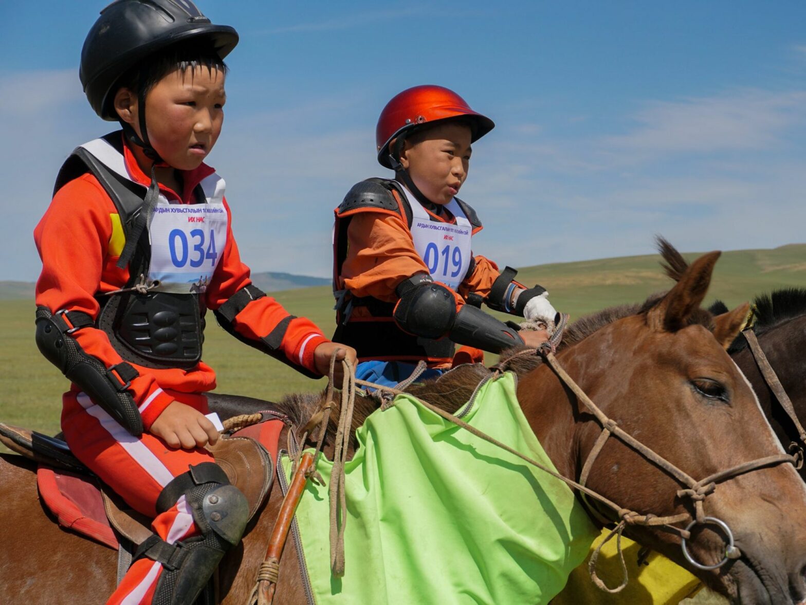 Two child jockeys in racing attire, on their horses, preparing to race.