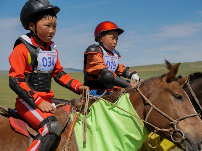 Two child jockeys in racing attire, on their horses, preparing to race.