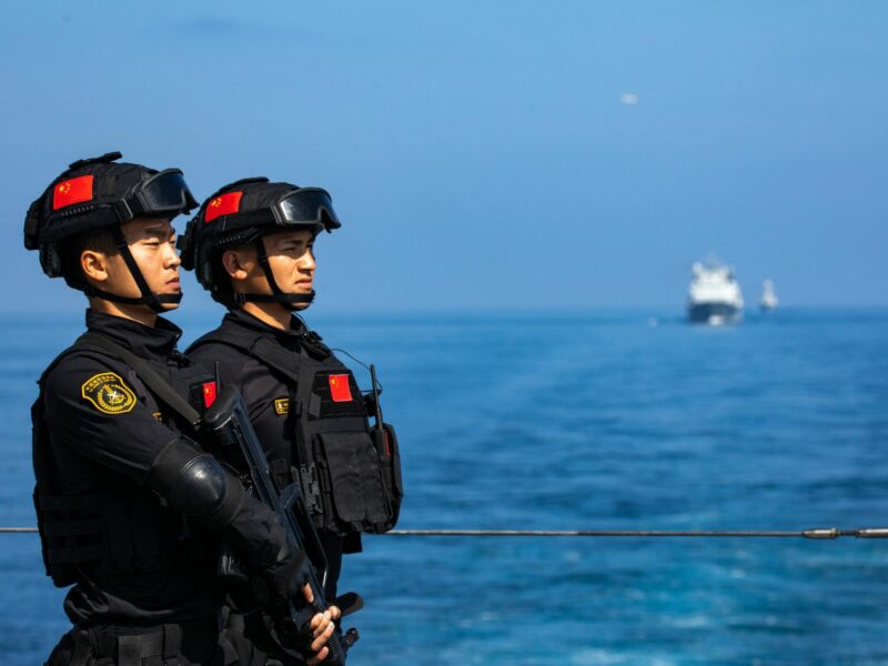 Two Chinese soldiers in black tactical gear stand on deck