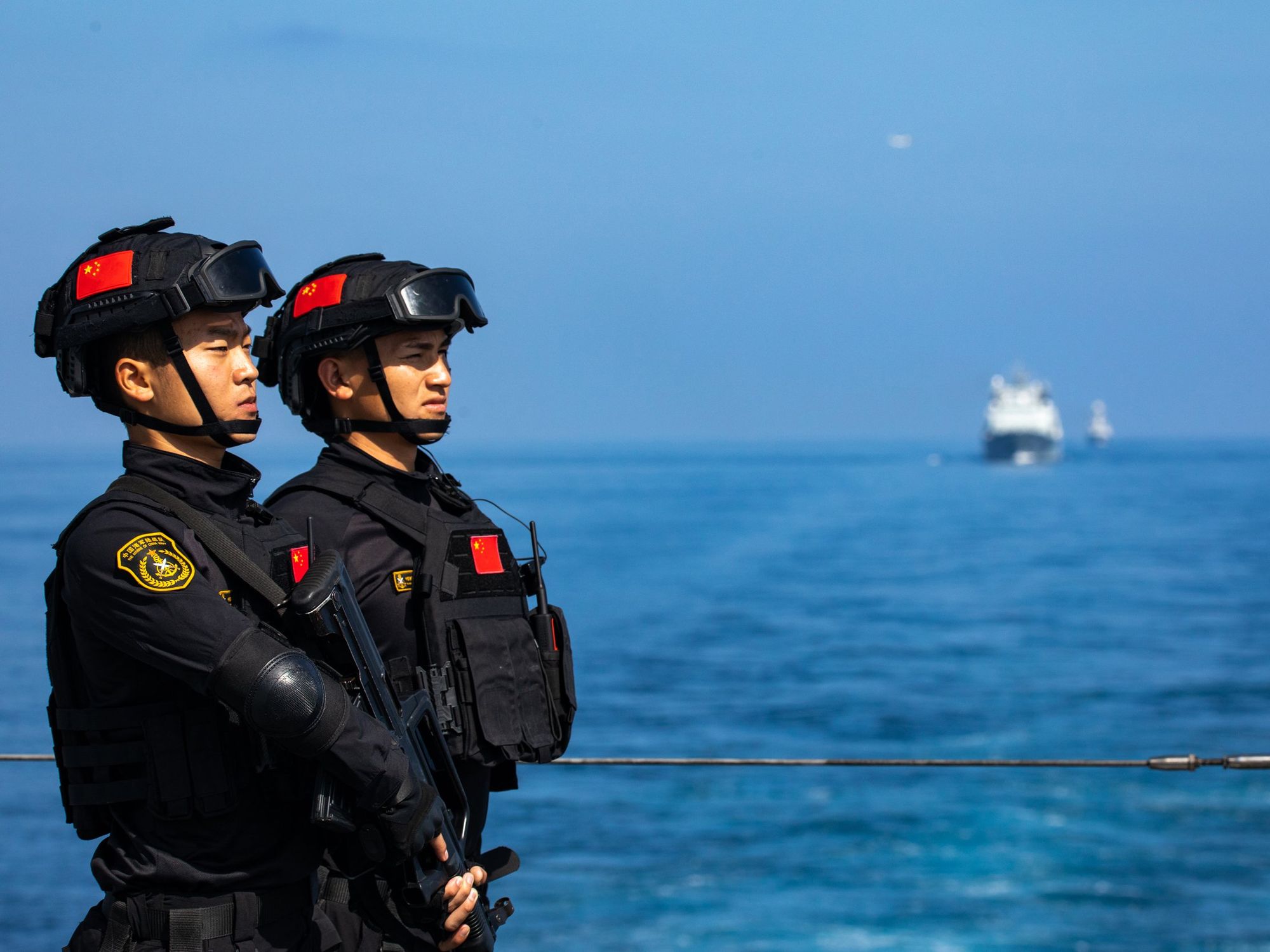 Two Chinese soldiers in black tactical gear stand on deck