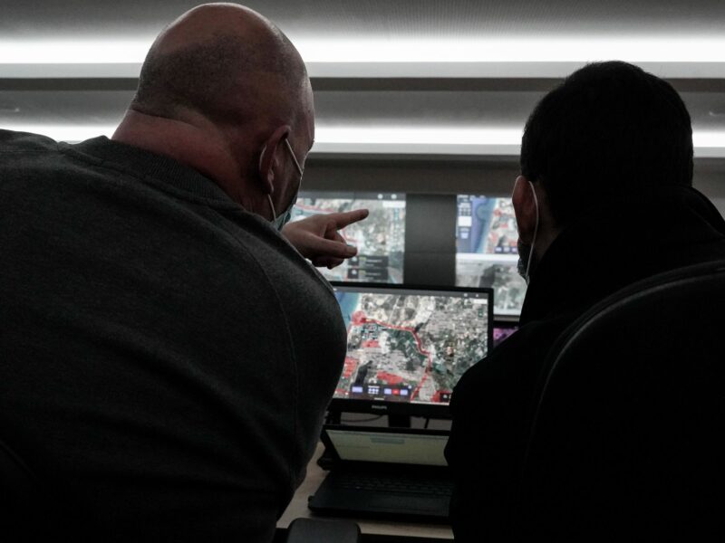 Two men look at various computer screens and point out details.