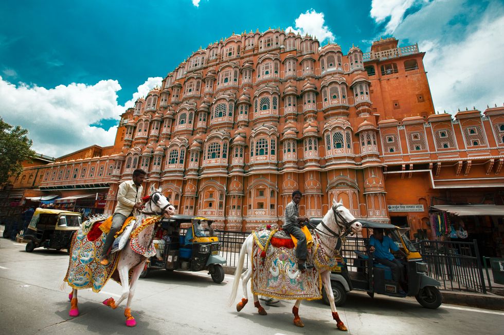 Two men riding their horses in front of an orange building.