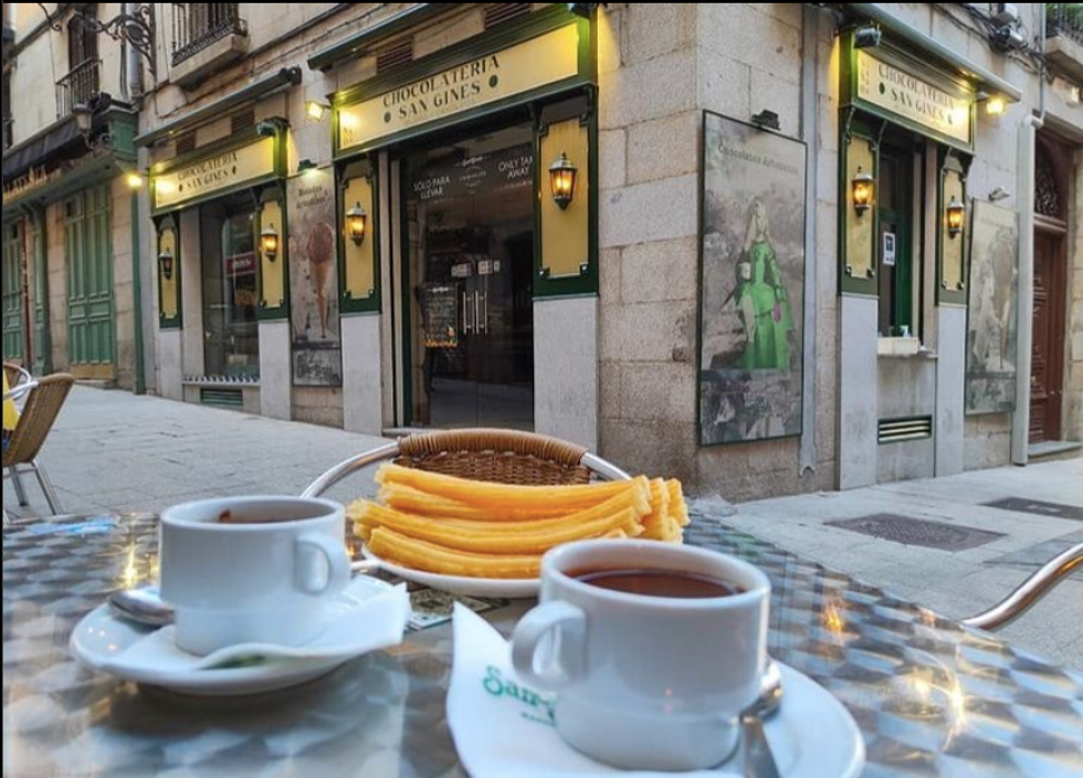 Two mugs of chocolate and a plate of churros outside of Chocolateria San Gines