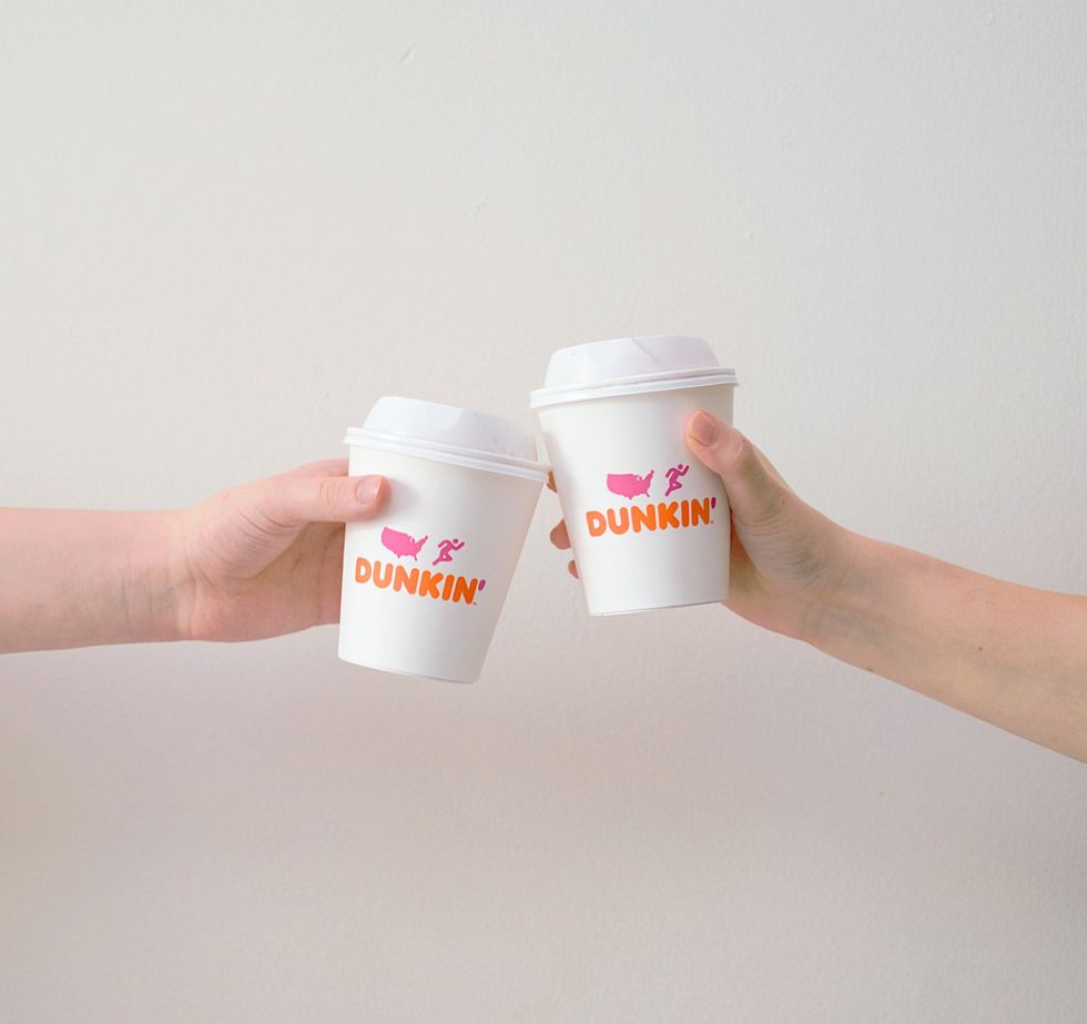 Two people holding Dunkin' coffee cups.