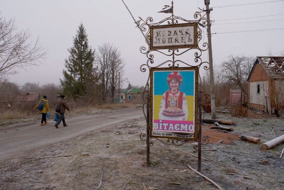 Two people walk down an abandoned street next to a colorful sign