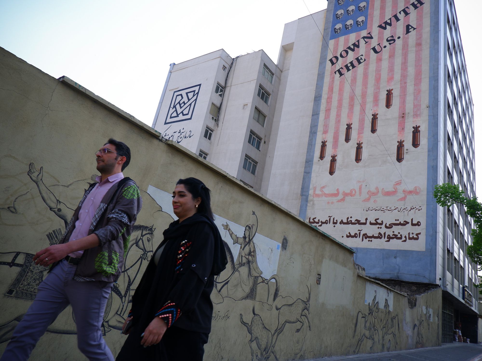 two people walking with a mural of american flag in background dropping bombs