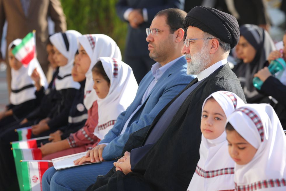 Two political leaders sit next to eachother with young veiled girls sitting besides them at a ceremony