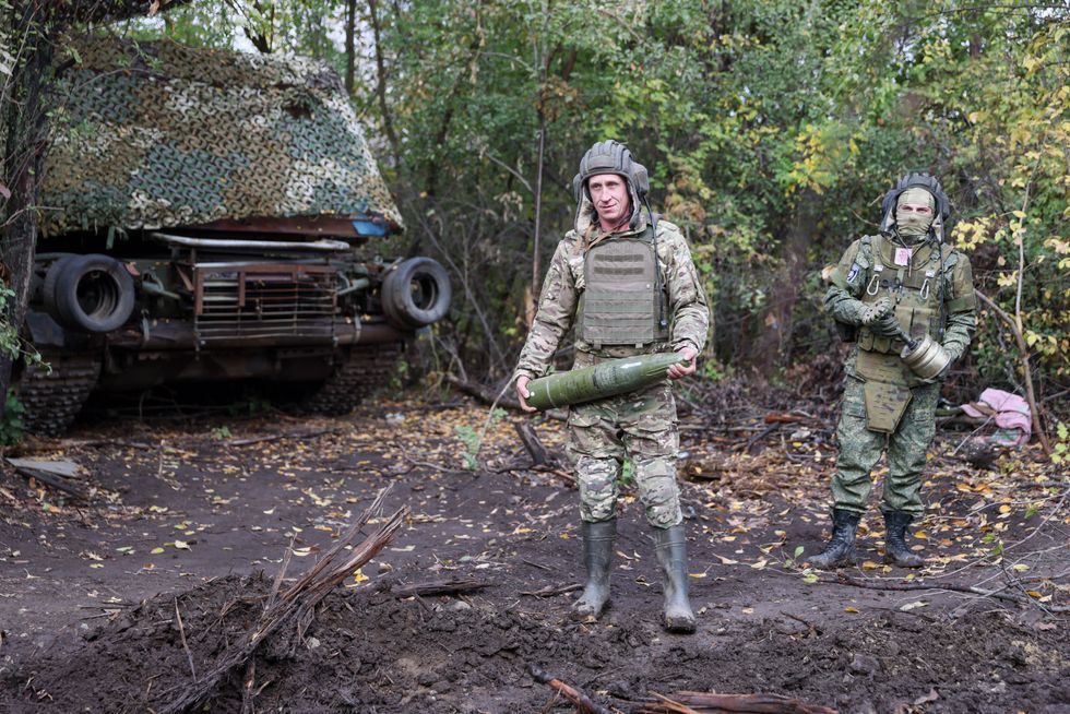 Two Russia soldiers are in the woods with an armored vehicle