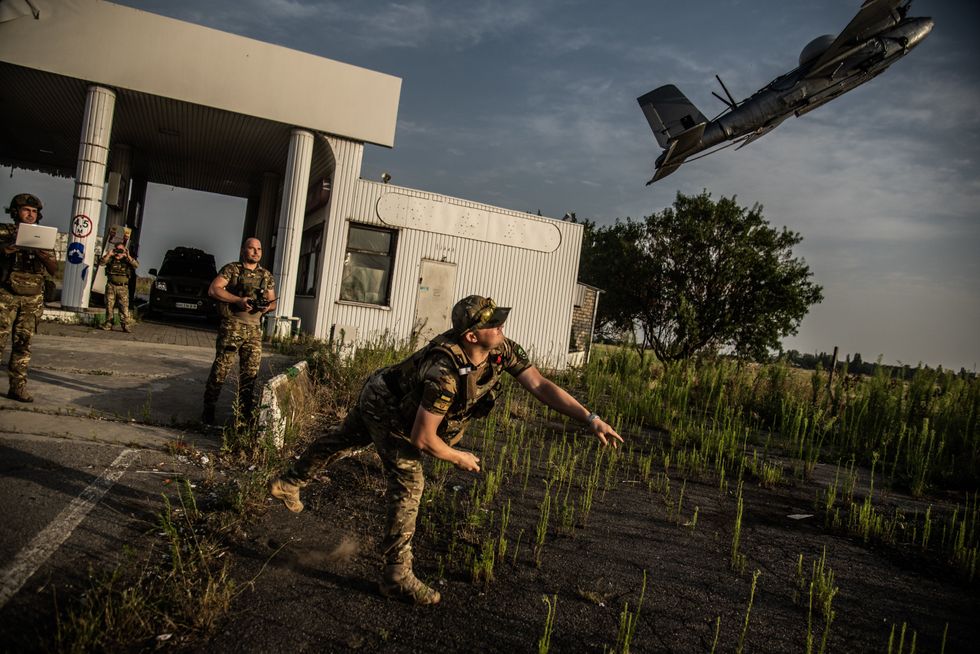 Two Soldiers are seen using technology to control a drone that was launched by a third soldier. A fourth soldier is taking a photo of the event.