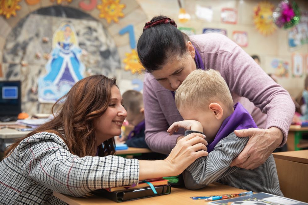 Two teachers calm a distraught boy from primary school during class.