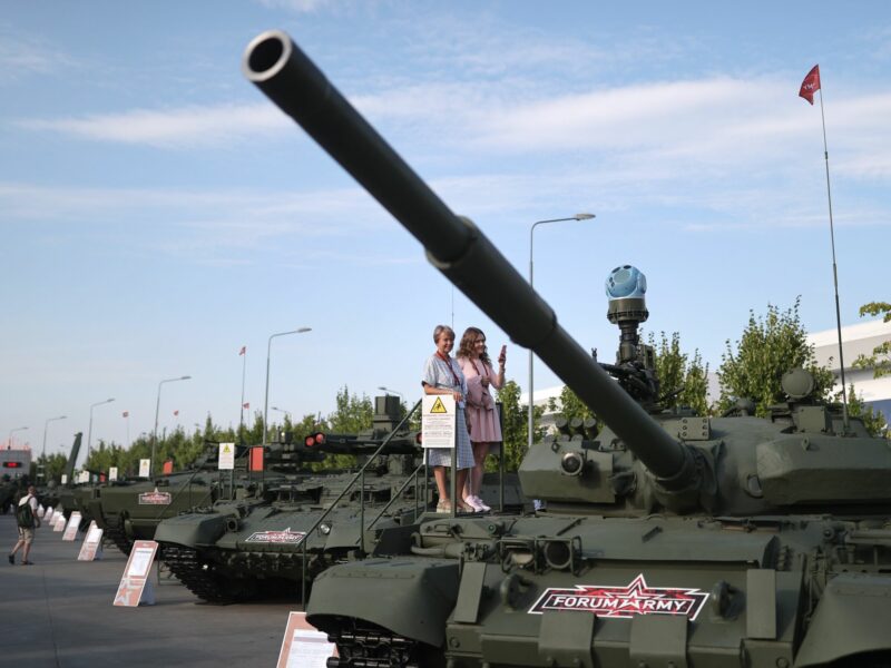 Two women look at a displayed tank from a platform
