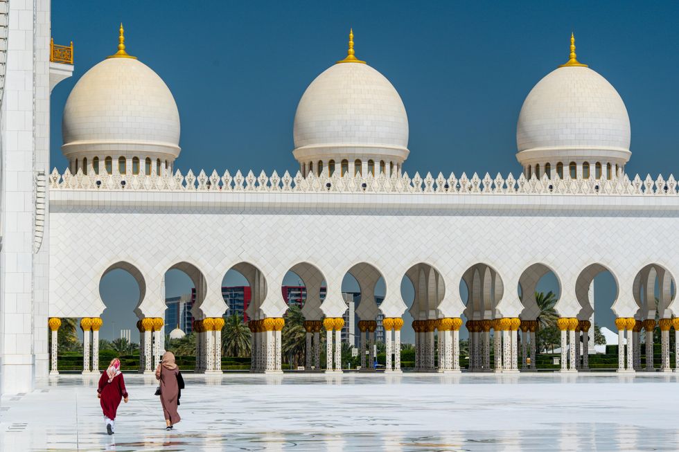 Two women walk in the courtyard of a mosque.