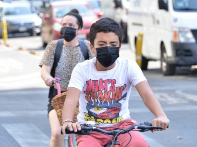 Two young ride a bike wearing protective face masks.