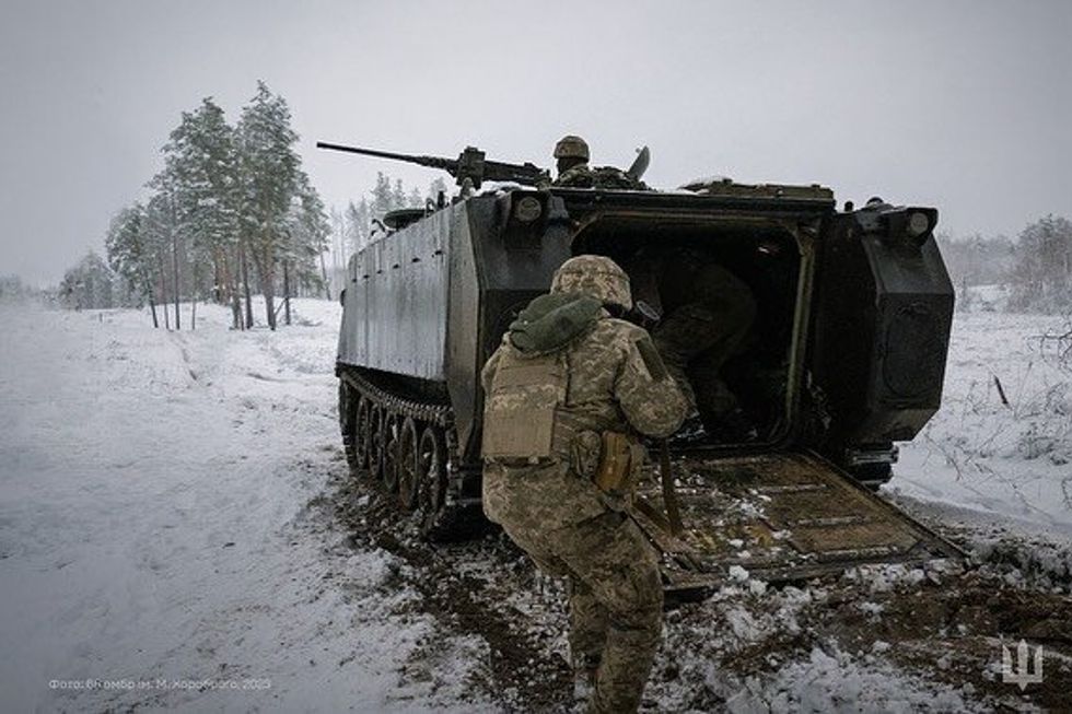 Ukraine soldier in winter moving to get in a tank while another Ukraine soldier is ontop the machine gun on the tank.