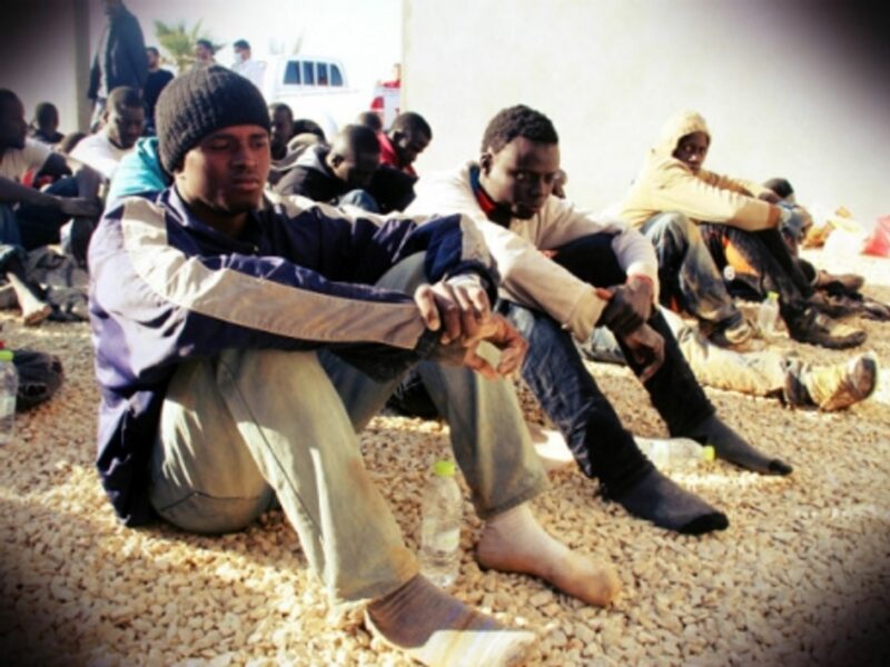 Undocumented immigrants sit in a yard guarded by Libyan police in Tripoli