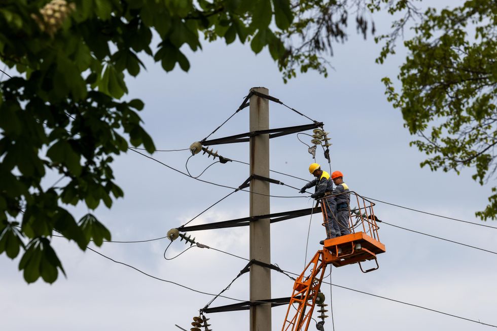 Utility workers use an access platform to repair damaged power lines in the city of Mariupol