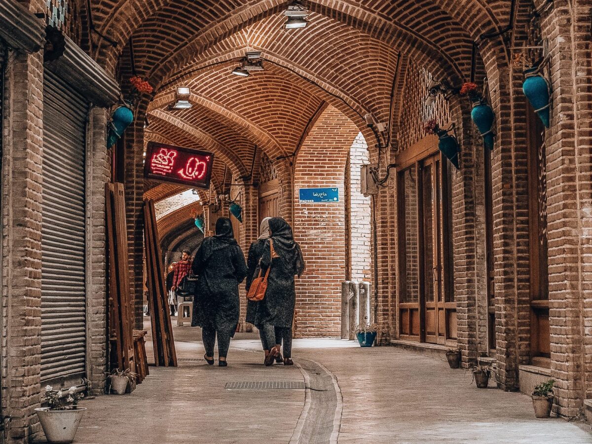 Veiled women walking down a brown arched concrete corridor.