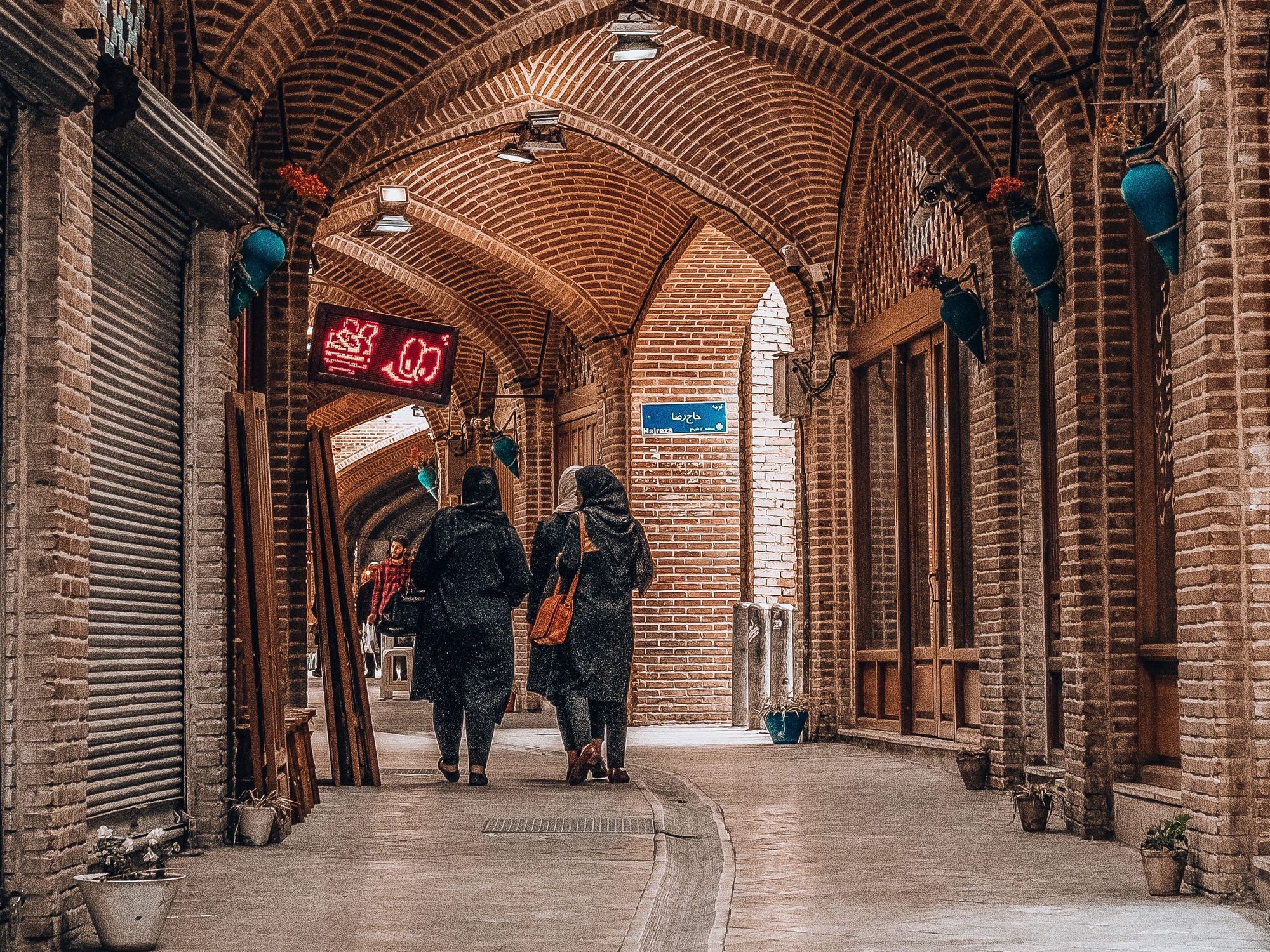 Veiled women walking down a brown arched concrete corridor.