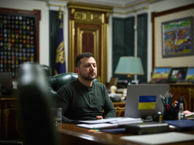 Volodymir Zelensky sits in his office while looking at a laptop with a Ukraine flag logo on the back
