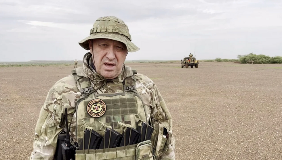 Wagner boss Yevgeny Prigozhin holding a rifle in a desert area while wearing camouflage.