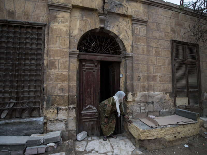 Women in Hijab bent over in front of a brick house