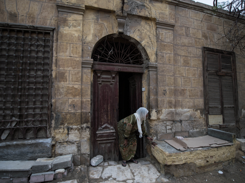 Women in Hijab bent over in front of a brick house