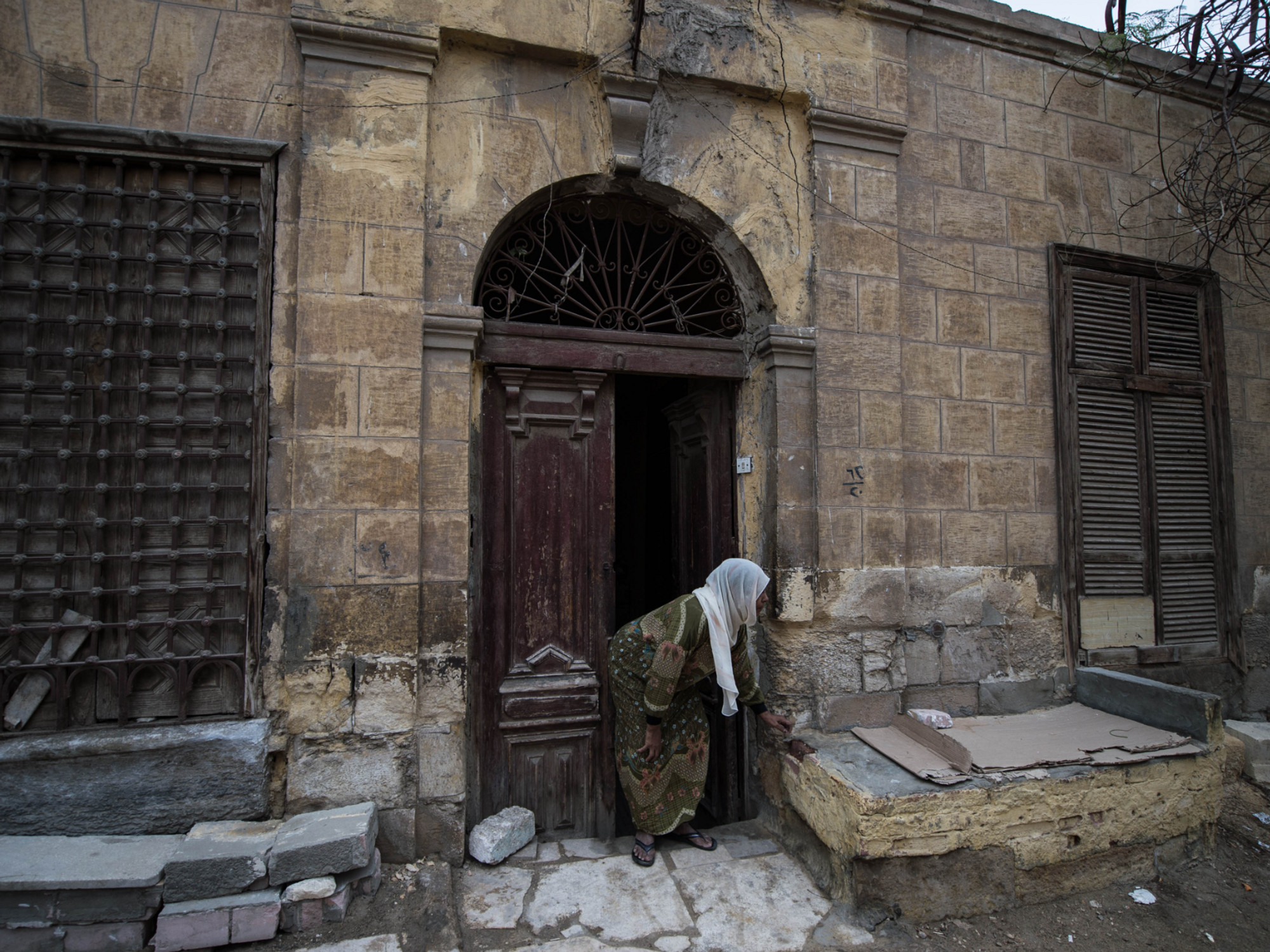 Women in Hijab bent over in front of a brick house