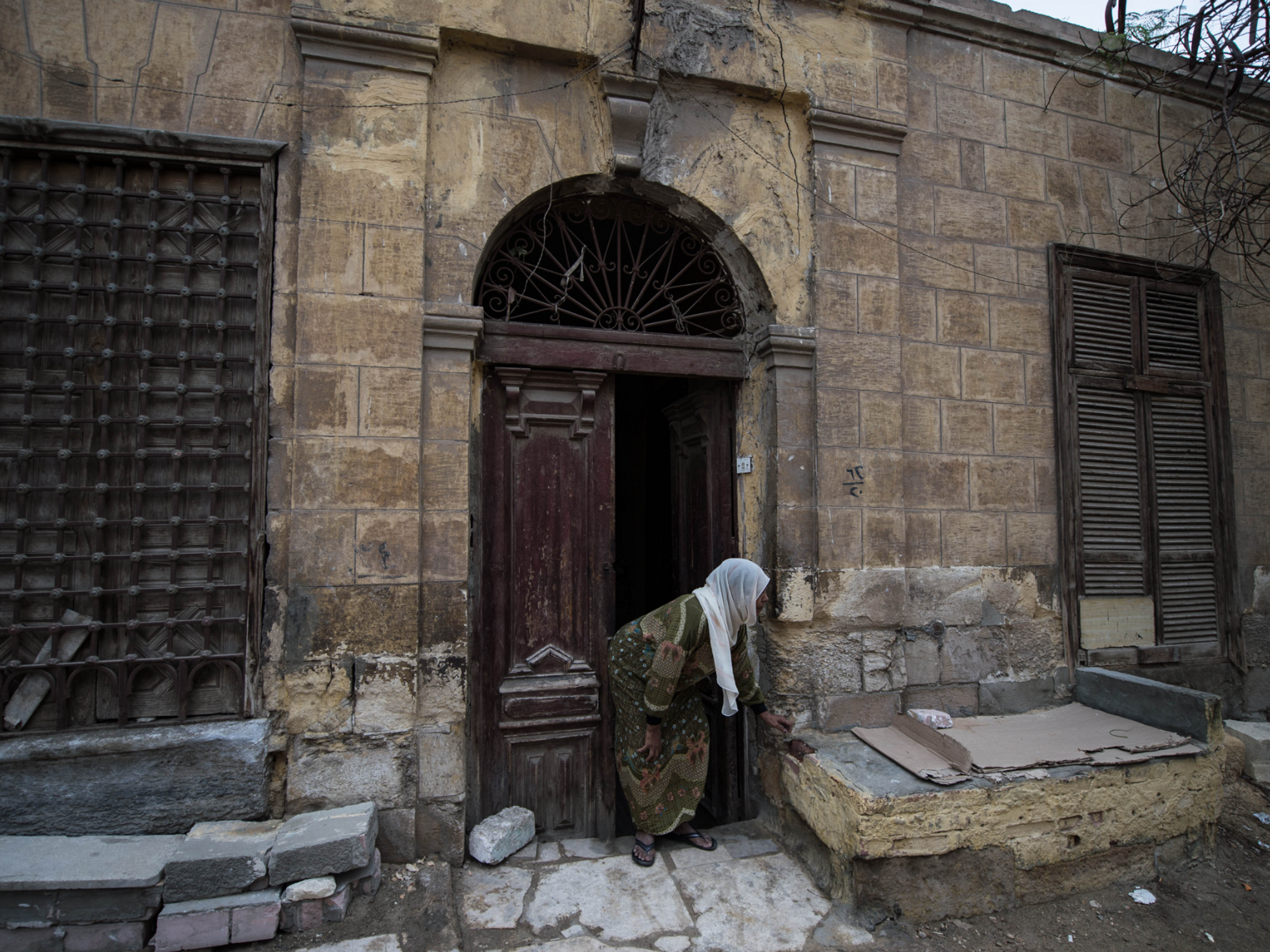 Women in Hijab bent over in front of a brick house
