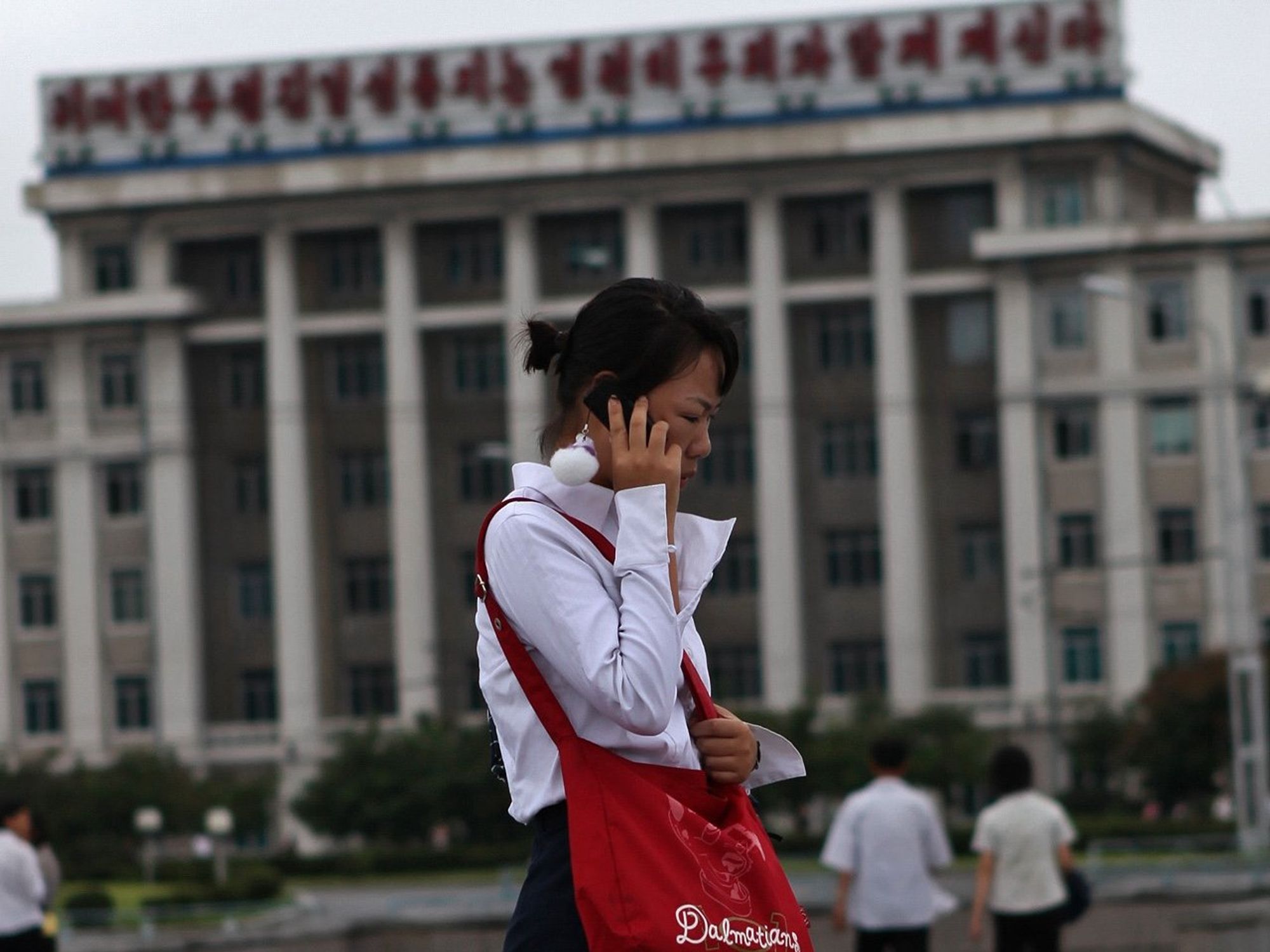 Women in Pyongyang on a phone call, she has a red bag and you can see people in the background.