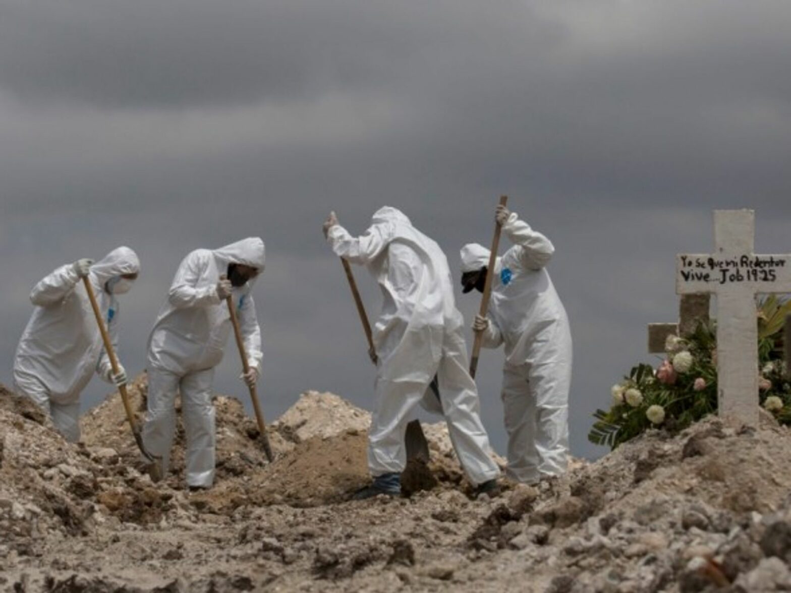 Workers in protective suits are shoveling earth at a funeral in Mexico, Tijuana.