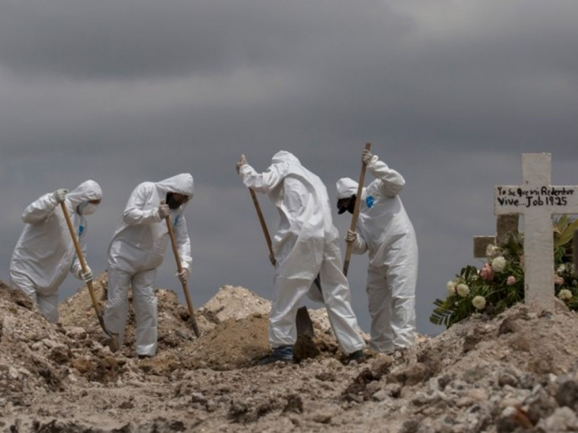 Workers in protective suits are shoveling earth at a funeral in Mexico, Tijuana.