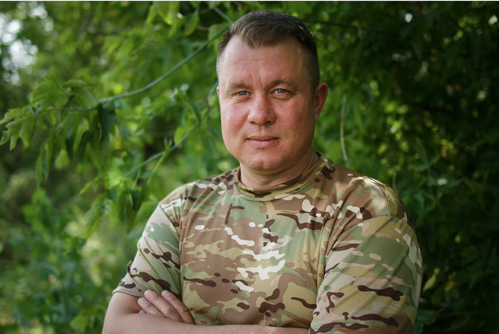 Yevhen Mezhevikin stands with his arms crossed infront of some foliage