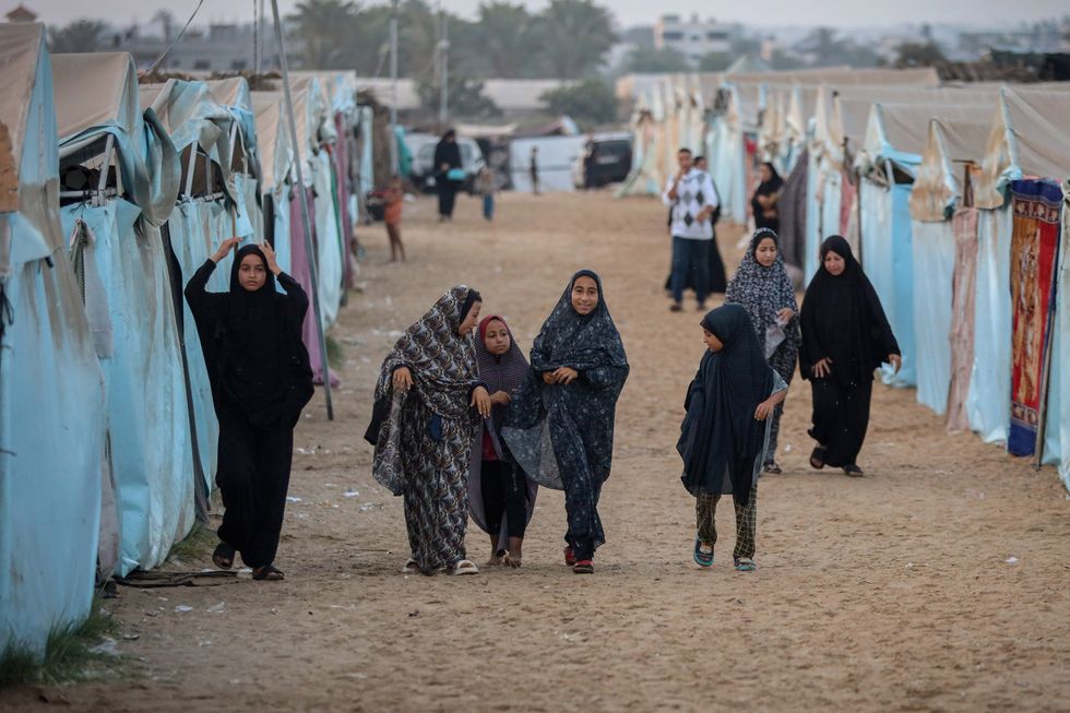 young women in hijabs walking down a street in between cloth houses with an older women in front
