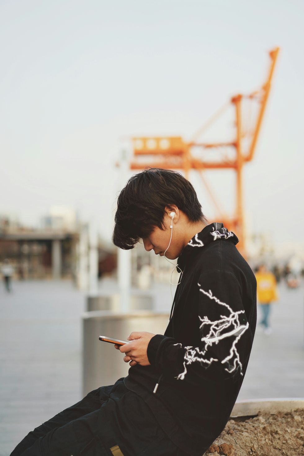 A man dressed in black is sitting on a wall, looking at his smartphone
