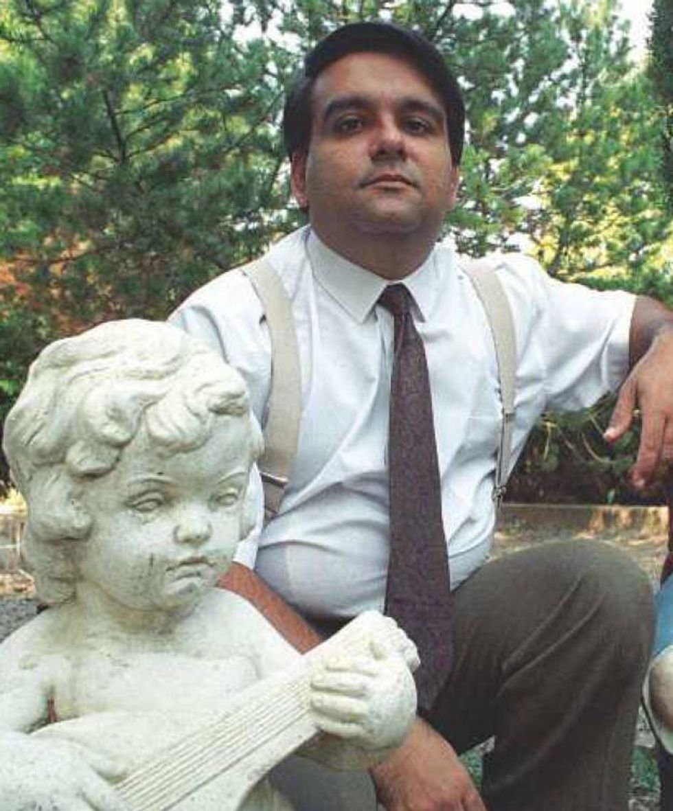 A spanish man wearing a dress shirt, tie, and suspenders is in a garden.