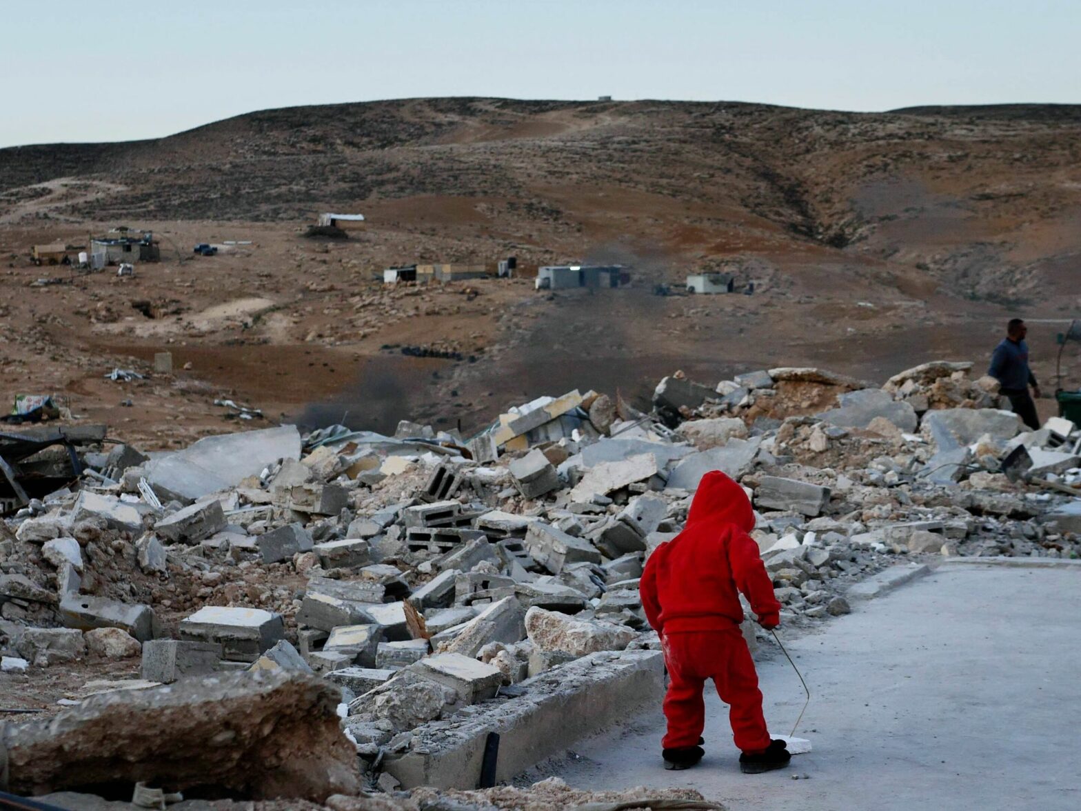 ​A child wearing red stands amidst rubble in a desolate field